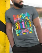 Everyone Communicates Differently Colorful Puzzle Graphic Tee - model wearing grey tee, leaning on column