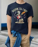 Rockin Till I Rot Skeleton Guitar Rock Music Graphic Tee Tshirt - model wearing navy tee with hands in pockets