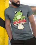 Happy Frog Sitting Mushroom Cartoon Graphic T Shirt Fun Vibe - model wearing grey tee, leaning on column